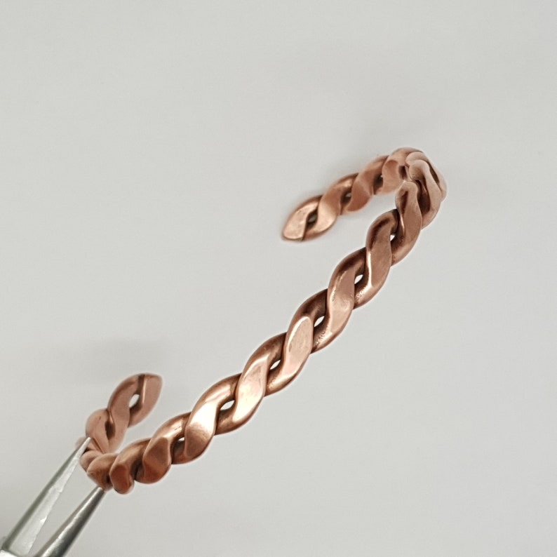 May include: A copper braided bangle bracelet. The bracelet is made from a single piece of copper wire that has been twisted and shaped into a bangle.