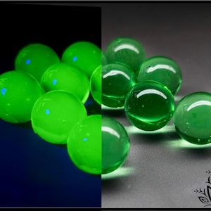 May include: A collection of smooth, spherical green glass marbles. The left side of the image shows the marbles glowing with a bright, neon green luminescence against a dark background, while the right side displays them in natural light.