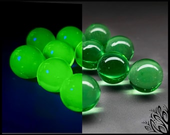 May include: A collection of smooth, spherical green glass marbles. The left side of the image shows the marbles glowing with a bright, neon green luminescence against a dark background, while the right side displays them in natural light.
