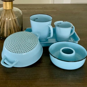 Pode incluir: Um conjunto de utensílios de cozinha de esmalte azul, incluindo um coador, uma tigela pequena, duas canecas e uma bandeja. As canecas são marcadas com "1/2 Litro" em letras pretas.