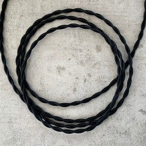 Könnte beinhalten: Schwarzes, gedrehtes Stromkabel, auf einer grauen Oberfläche aufgerollt.