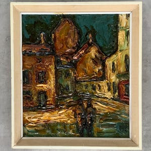 May include: An oil painting in a light wood frame depicting a street scene with textured, thick brushstrokes. The composition features brown and yellow buildings against a dark teal sky, with two dark figures walking in the foreground.