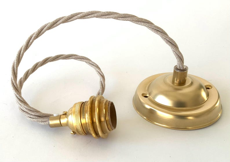 May include: A brass-colored pendant light fixture with a twisted, beige fabric cord. The fixture includes a bulb socket and a ceiling canopy. The components are arranged on a white surface.