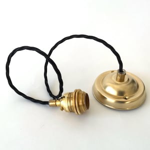 以下が含まれることがあります： 真鍮色のペンダントライト器具と黒色のねじれたコード。器具には電球ソケットと円形のシーリングキャノピーが含まれています。コンポーネントは白い背景に配置されています。