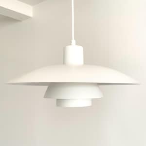 May include: A matte white pendant light fixture featuring a tiered design with three distinct circular shades of varying sizes stacked vertically. The fixture is suspended by a single thin white cord attached to a cylindrical top housing component.