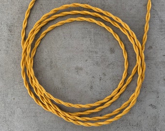 May include: A close-up of a gold braided cord, twisted into a circle. The cord is thick and has a textured surface.