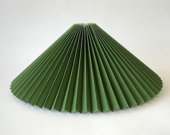 Puede incluir: Pantalla de lámpara plisada verde con forma cónica. Hecha de papel o tela, presenta pliegues verticales que crean una superficie texturizada. Diseñada para difundir la luz, añade un elemento decorativo a una lámpara. Diámetro aproximado de 30 cm.