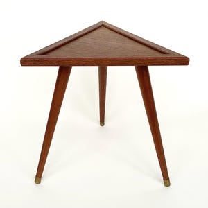 May include: A mid-century modern triangular side table. The table has a dark brown wooden top and three slender, tapered legs. The legs are also brown and have brass tips. The table is approximately 24 inches wide.