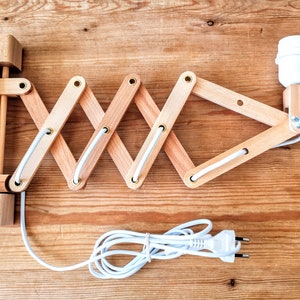 Puede incluir: Una l&aacute;mpara de pared de madera con un cable blanco y una toma de bombilla blanca. La l&aacute;mpara tiene un dise&ntilde;o plegable y se puede ajustar a diferentes &aacute;ngulos.