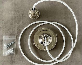 May include: A ceiling light fixture kit with a silver-colored canopy and a matching decorative cap. The kit includes a white, twisted fabric-covered cord and a small bag of screws and anchors. The components are arranged on a gray surface.