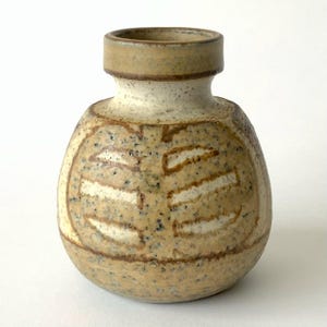 May include: A small, round ceramic vase with a speckled beige and tan glaze. The vessel features a short, cylindrical neck and a wide, bulbous body decorated with incised, horizontal white-filled lines arranged in a symmetrical pattern.