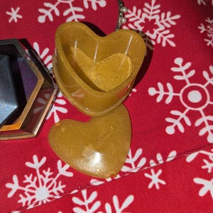 May include: A gold heart-shaped trinket box with a lid. The box is made of resin and has a glittery finish.