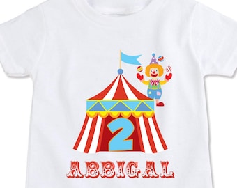 May include: White t-shirt with a red and white striped circus tent, a clown juggling balls, and the number 2. The text "ABBIGAL" is below the tent.  Personalize with any Name/Age!