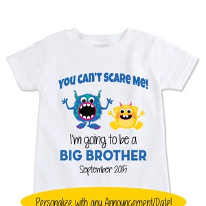 May include: White t-shirt with a blue and yellow monster graphic. The text reads "You can't scare me! I'm going to be a big brother September 2015".