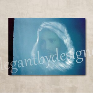 May include: A faded blue photograph of a person's face, partially obscured by a white cloud-like shape. The image is slightly blurred and has a vintage feel.