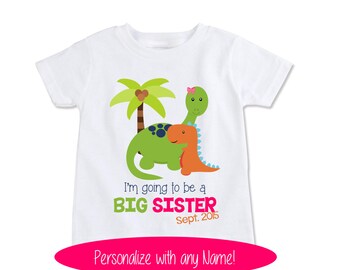 Op de afbeelding: Wit T-shirt met een groen en oranje dinosaurusontwerp. De tekst "I'm going to be a BIG SISTER Sept. 2015" staat op het shirt gedrukt.