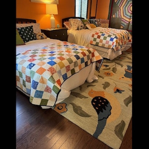 Könnte beinhalten: Zwei Einzelbetten mit karierten Bettdecken in einem Schlafzimmer mit orangefarbener Wand. Die Betten haben weiße Laken und Kissen. Ein Teppich mit einem Vogelmuster liegt auf dem Boden.