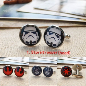 May include: A set of round silver-toned cufflinks featuring various Star Wars character and symbol designs. The designs include a white Stormtrooper helmet, a red Rebel Alliance symbol, a black Darth Vader mask, and a red Galactic Empire symbol.