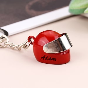 Puede incluir: Llavero de casco de moto rojo con visera plateada y el nombre "Adam" grabado en el lateral.