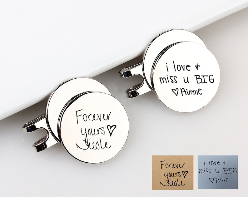 May include: Two silver-colored, round pendants with handwritten inscriptions. One says "Forever yours Nicole" and the other says "i love + miss u BIG Aimme". The pendants have a clasp design.