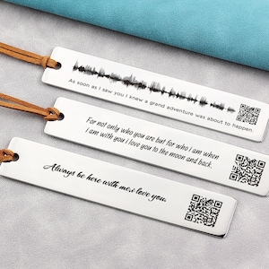 May include: Three silver bookmarks with brown leather cords. The bookmarks have engraved text and a QR code. The text reads: "As soon as I saw you I knew a grand adventure was about to happen." "For not only who you are but for who I am when I am with you I love you to the moon and back." "Always be here with me, I love you."