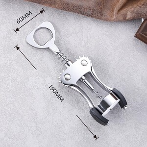 K&ouml;nnte beinhalten: Ein polierter Wein&ouml;ffner aus Chrom mit einem Flaschen&ouml;ffner, der 19 cm lang und 6 cm breit ist. Der &Ouml;ffner hat ein Hebeldesign mit schwarzen Gummi-Griffen und einem Korkenzieher. Das Werkzeug dient zum &Ouml;ffnen von Weinflaschen.