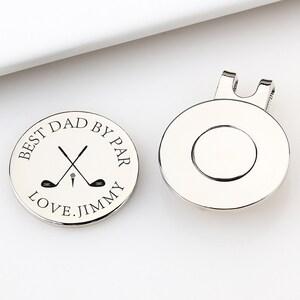 May include: Two silver golf ball markers. One marker has the text "BEST DAD BY PAR LOVE. JIMMY" around a crossed golf club and tee design. The other marker has a magnetic clip on the back. Golf-themed gift.
