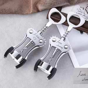 May include: Two silver wine corkscrews with black accents. One corkscrew has the text "Je t'aime" and a heart, the other has "Love Jimmy". The corkscrews have a bottle opener design.