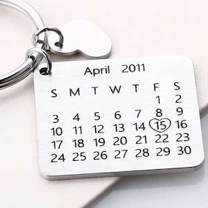 May include: Silver keyring with a heart charm and a calendar engraved with the date April 15, 2011. The number 15 is highlighted with a heart.