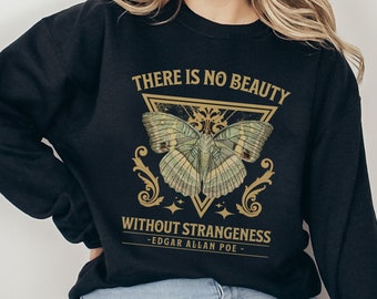 Puede incluir: Sudadera negra con un gráfico dorado de una mariposa dentro de un triángulo. El texto "There is no beauty without strangeness - Edgar Allan Poe -" está impreso debajo de la mariposa.