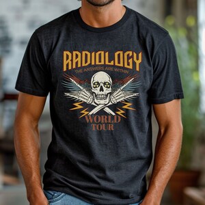 Op de afbeelding: Een zwart T-shirt met een vintage grafisch ontwerp met een schedel met vleugels en de tekst "Radiologie: De antwoorden liggen binnenin" en "World Tour".