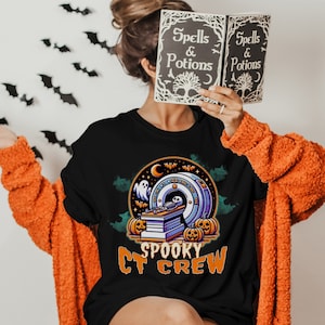 Könnte beinhalten: Ein schwarzes T-Shirt mit einem gruseligen CT-Crew-Design. Das Design zeigt ein Skelett in einem CT-Scanner mit Kürbissen und Fledermäusen. Der Text "Spooky CT Crew" ist unter dem Design gedruckt.