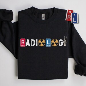 May include: Black sweatshirt with the word "RADIOLOGY" in white, with the letters "RAD" and "TECH" in red and blue rectangles. The letter "O" is a yellow radiation symbol, and the letter "G" is a skeleton hand making a peace sign.