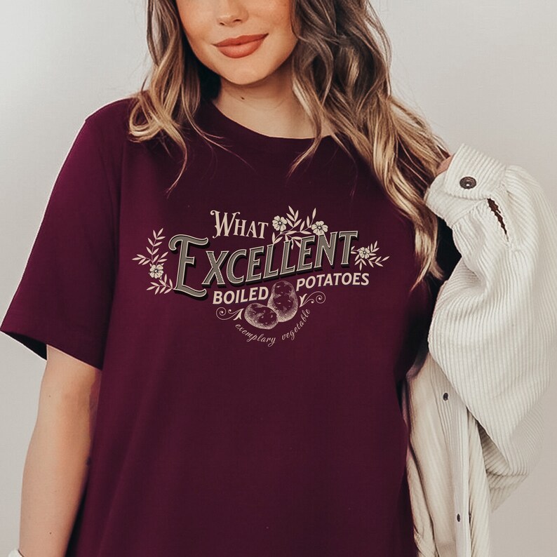 May include: A maroon t-shirt with a vintage-style graphic that reads "What Excellent Boiled Potatoes, exemplary vegetable". The graphic features a stylized illustration of potatoes and floral accents.
