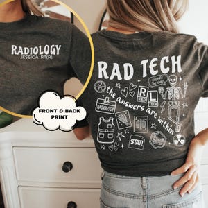 May include: Dark gray t-shirt with white text and graphics. The front says "RADIOLOGY" and "JESSICA RT(R)". The back features "RAD TECH" and medical-themed illustrations, including a skeleton and the phrase "the answers are within."