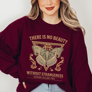 May include: Burgundy sweatshirt with a gold butterfly graphic and the quote "There is no beauty without strangeness - Edgar Allan Poe -"