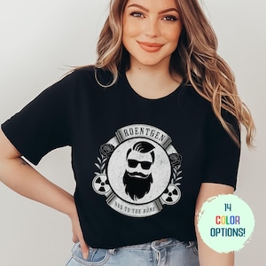 May include: Black t-shirt with a white graphic of a bearded man wearing sunglasses and a mustache. The graphic is surrounded by a circle with the text "Roentgen Bad to the Bone".