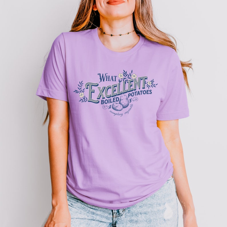 May include: A light purple t-shirt with the text "What Excellent Boiled Potatoes" in a vintage-style design. The graphic includes illustrations of potatoes and floral accents. The shirt is made of a soft material.