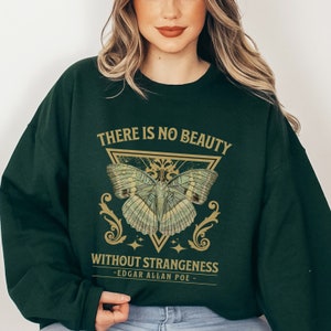 May include: A dark green sweatshirt with a gold graphic of a butterfly inside a triangle. The text "THERE IS NO BEAUTY WITHOUT STRANGENESS - EDGAR ALLAN POE -" is printed below the butterfly.