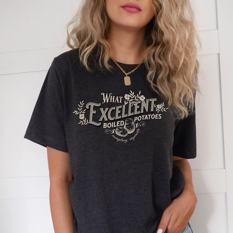 May include: A dark gray t-shirt with a vintage-style graphic that reads "What Excellent Boiled Potatoes" with a floral design and the words "Exemplary Vegetable".