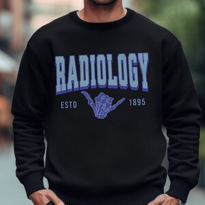 May include: Black sweatshirt with a blue and white graphic print that says "RADIOLOGY ESTD 1895" with a skeleton hand making a shaka sign.