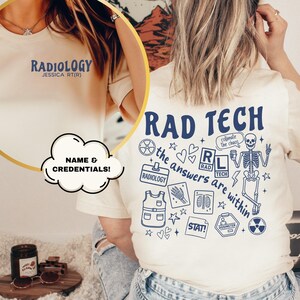 May include: Cream-colored t-shirt with blue text and graphics. The front says "RADIOLOGY" and "JESSICA RT(R)". The back features "RAD TECH" and medical-themed illustrations, including a skeleton and the phrase "the answers are within".