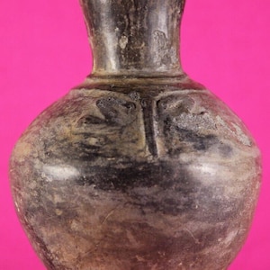 May include: A dark, antique-looking vase with a rounded body and a narrow neck. The vase has a weathered appearance with a dark, mottled color scheme, possibly indicating age or a specific firing technique. The surface shows subtle textures.