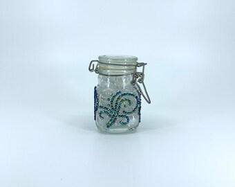 Airtight glass storage jar, clasp lid. AB black Diamond Dotz. Jar has four sides with a swirl design on each. 3 1/2 in. high, 1 1/2 in. wide
