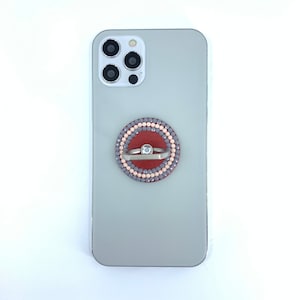May include: A gray phone case with a red, pink, and gray beaded phone ring holder.