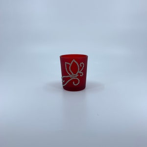 May include: Red glass candle holder with a white floral design.