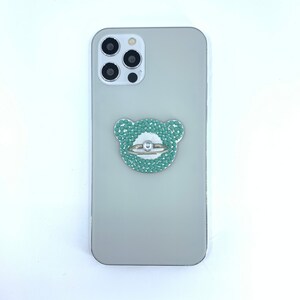 May include: A light gray phone case with a green and white bear-shaped phone ring holder with rhinestones.