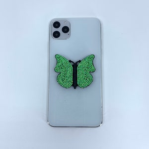May include: A white smartphone with a green and black butterfly phone grip attached to the back.
