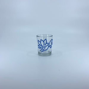 May include: A clear glass votive candle holder with a blue floral design. The design is made of small blue beads.