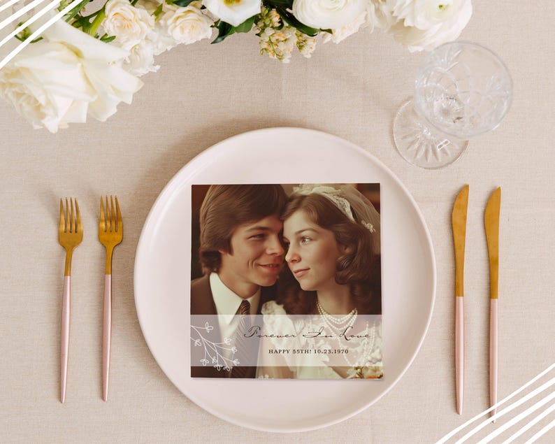 May include: A square photo card with a vintage couple photo, text reading "Forever in Love" and "Happy 55th! 10.23.1970". The card sits on a white plate, with gold and pink cutlery, and a glass. White flowers are in the background.